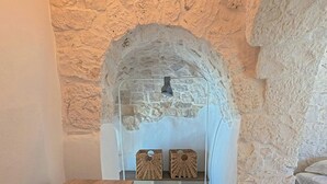 A room with a stone wall, a wooden desk, a cushioned chair, and a bed with white bedding. - Trullo with infinity pool amid olive groves (Alberobello)
