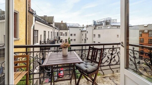 Ein Balkon mit Tisch und Stühlen, einem Blumentopf und Blick auf benachbarte Gebäude.