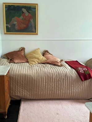 Una camera da letto con un letto, cuscini, un quadro, un comodino in legno e un tappeto.