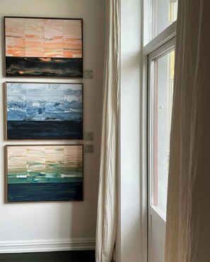 A hallway with three abstract paintings on the wall, a window with curtains, and a door. - Classic flat with balcony in St. Hanshaugen (Oslo)