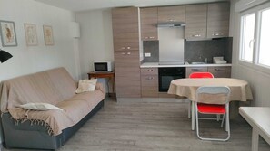 Ein kompakter Wohnraum mit einer Küchenzeile, einer Essecke mit Tisch und Stühlen, einem Sofa und einem Fernseher.