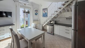 A modern kitchen with a dining table, chairs, a staircase, and a refrigerator. - Casa Nuvola (Senigallia)