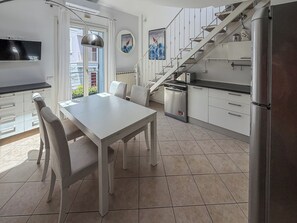 A modern kitchen with a dining table, chairs, a staircase, and a refrigerator. - Casa Nuvola (Senigallia)