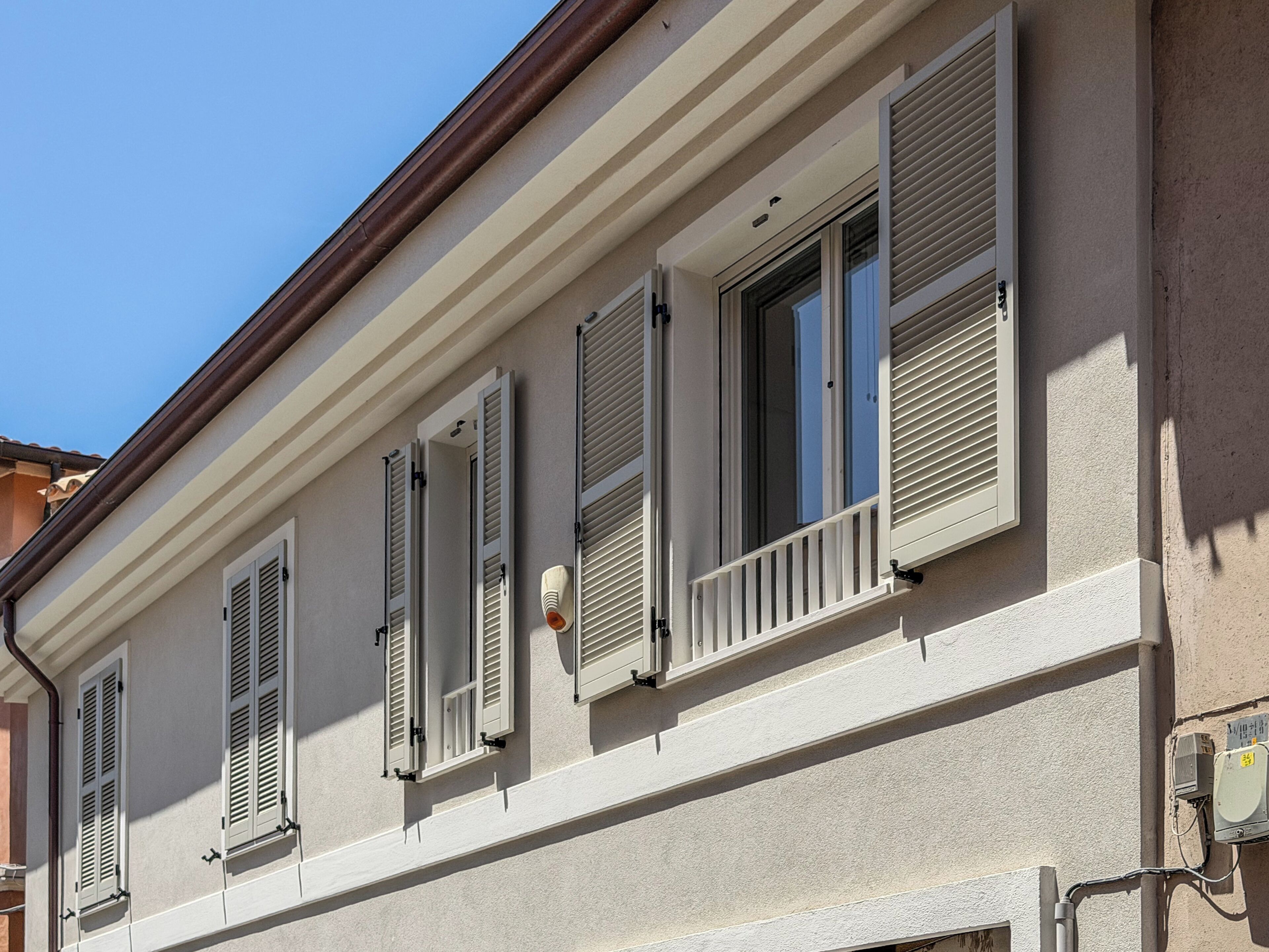 Fachada de edifício com várias janelas, persianas e unidade de ar condicionado visível.