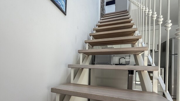 A modern staircase with wooden steps and white balusters, leading to a kitchen area with stainless steel appliances. - Casa Nuvola (Senigallia)