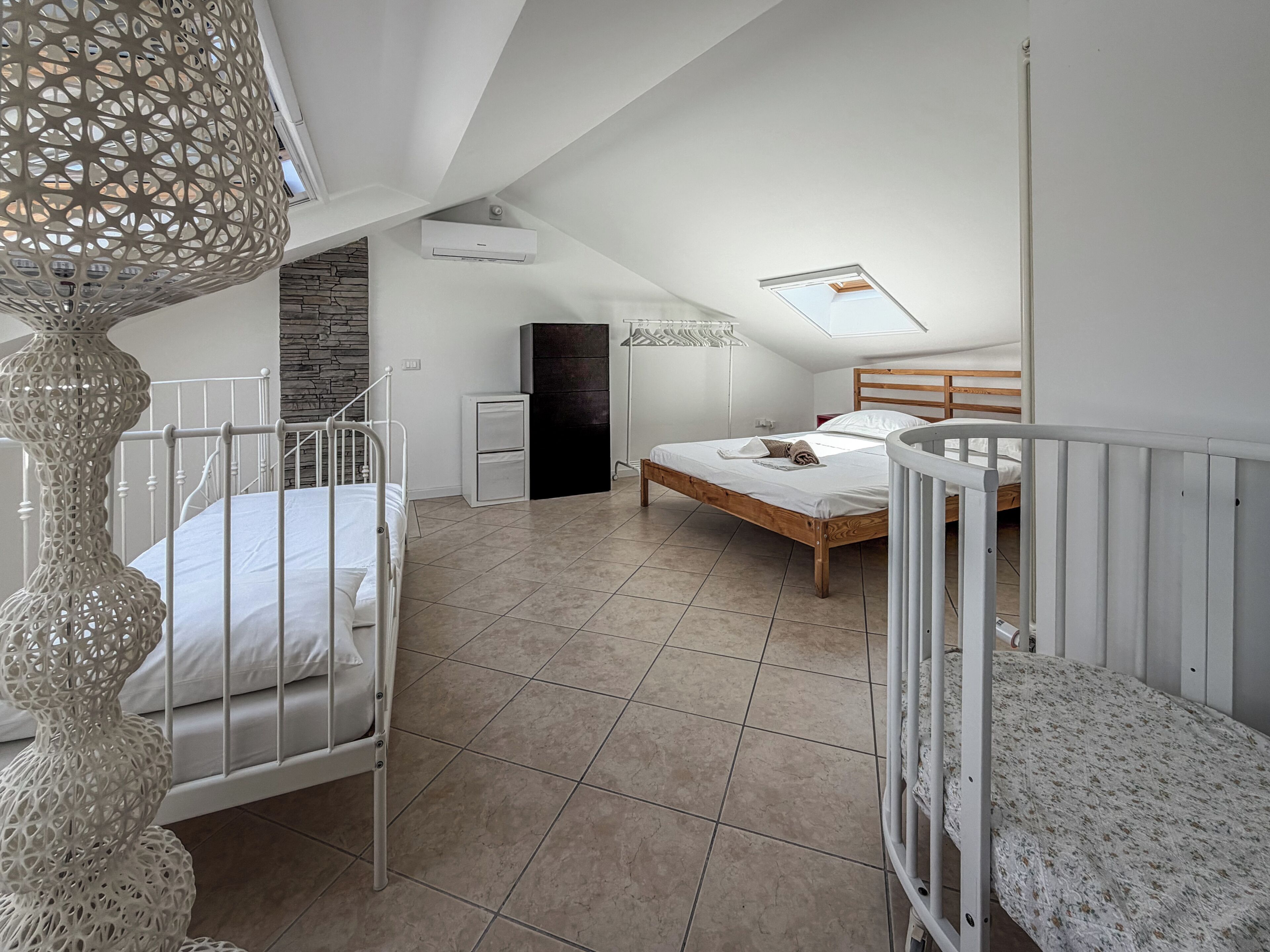 A bedroom with a sloped ceiling, a skylight, a bed, a dresser, and a white railing.