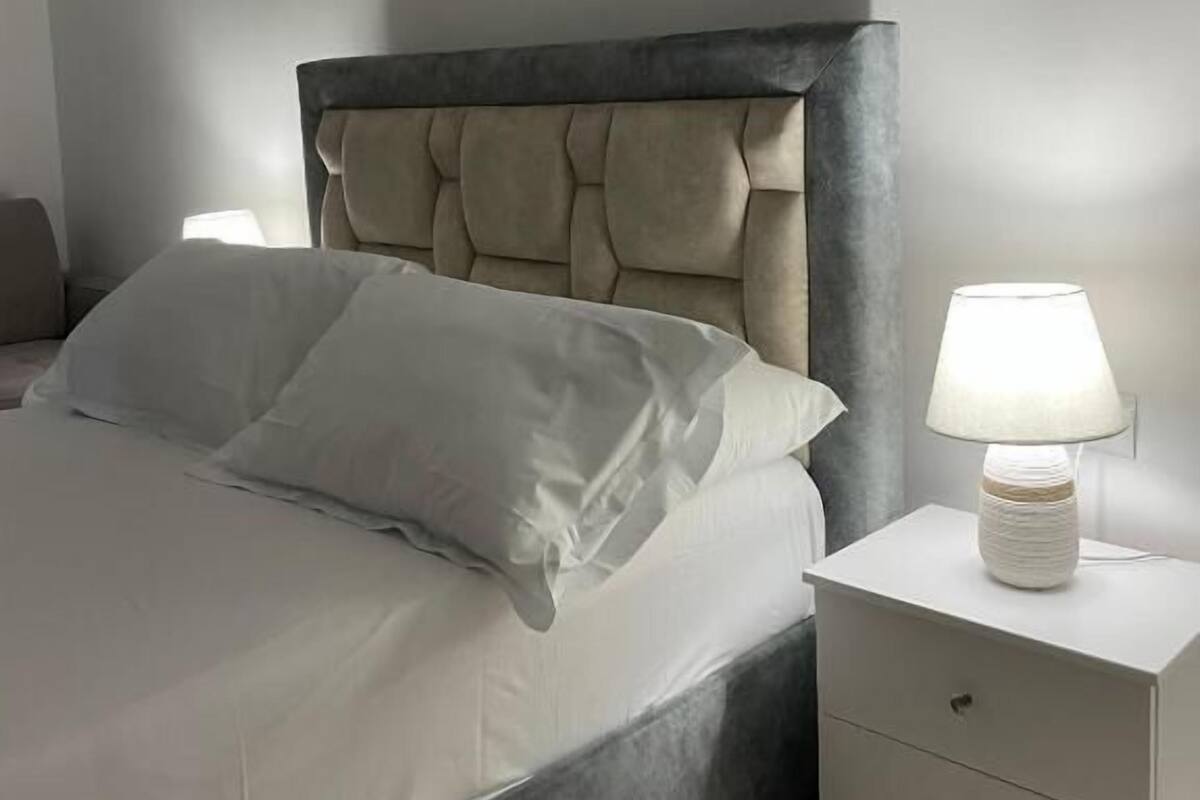 A bed with a tufted headboard, a bedside table with a lamp, and a nightstand with drawers.