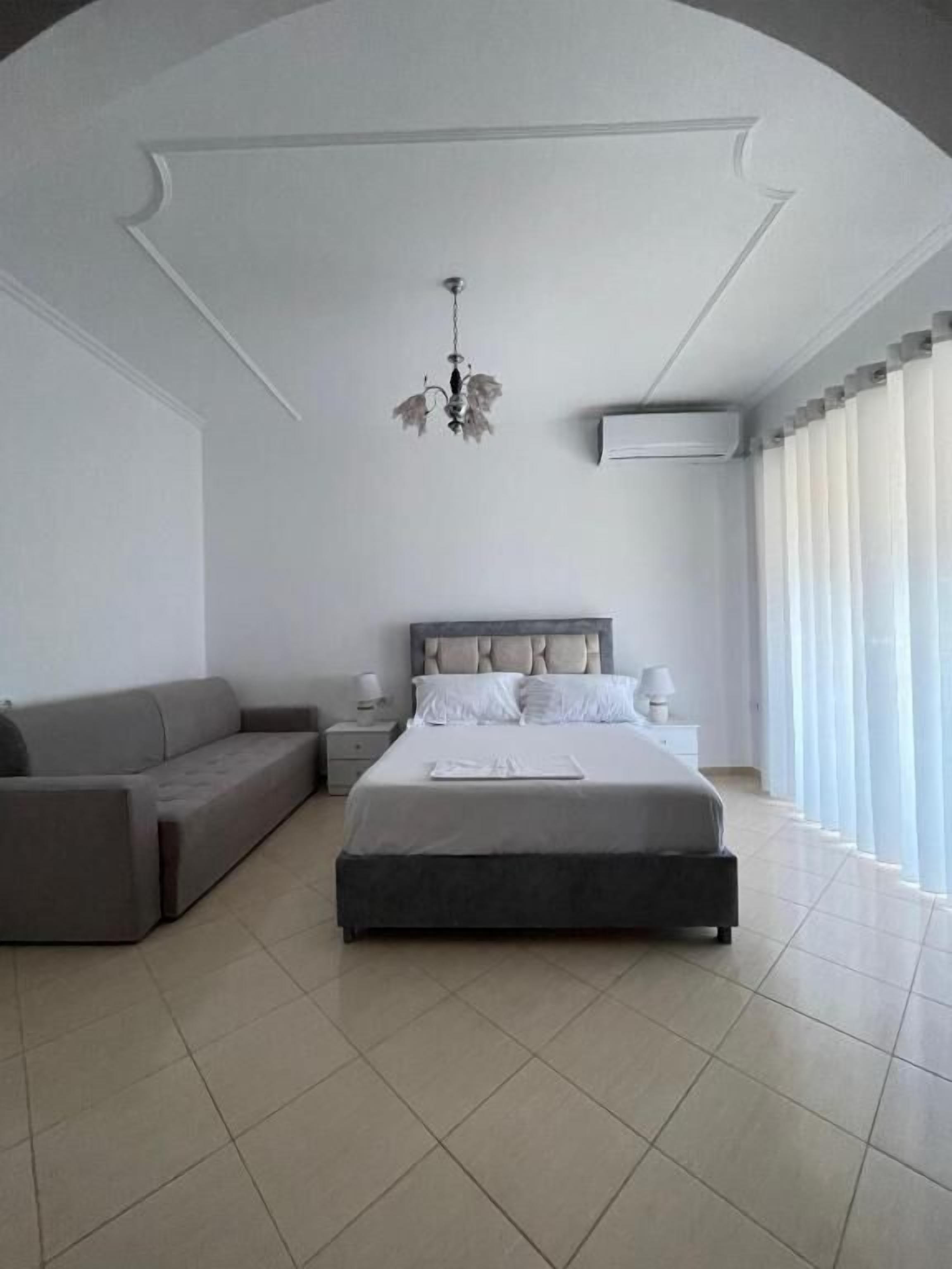 A modern bedroom with a large bed, a sofa, a nightstand, and a chandelier.