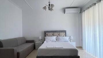 A modern bedroom with a large bed, a sofa, a nightstand, and a chandelier.