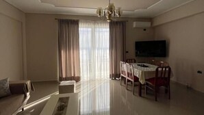 A living room with a sofa, coffee table, dining table, chairs, and a TV. - SeaSide Apartments (Sarande)
