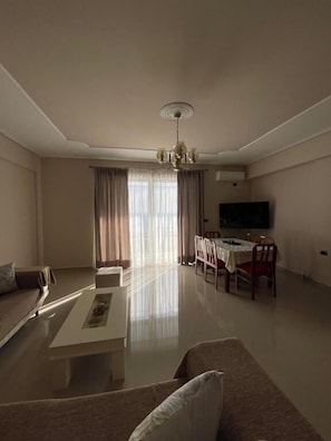 A living room with a sofa, coffee table, dining table, chairs, and a TV. - SeaSide Apartments (Sarande)