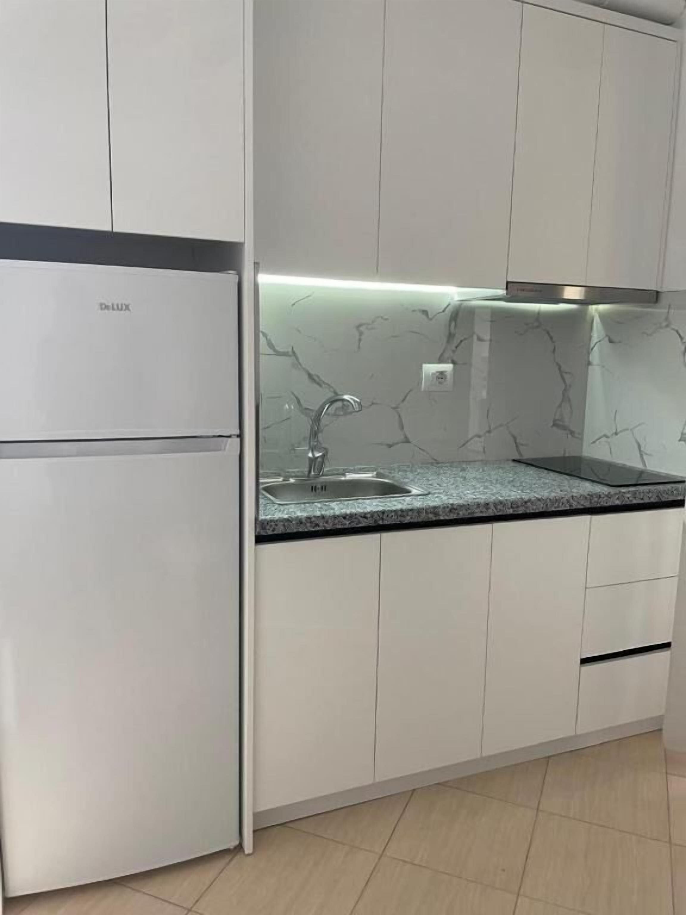 Una cocina con armarios blancos, salpicadero de mármol y refrigerador empotrado.