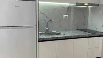 Una cocina con armarios blancos, salpicadero de mármol y refrigerador empotrado.