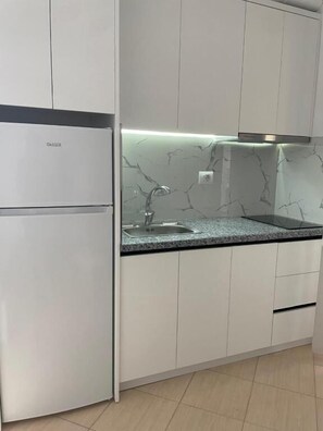 A kitchen with white cabinets, a marble backsplash, and a built-in refrigerator. - SeaSide Apartments (Sarande)
