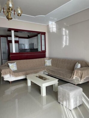 A living room with a sectional sofa, a coffee table, and a small ottoman. - SeaSide Apartments (Sarande)