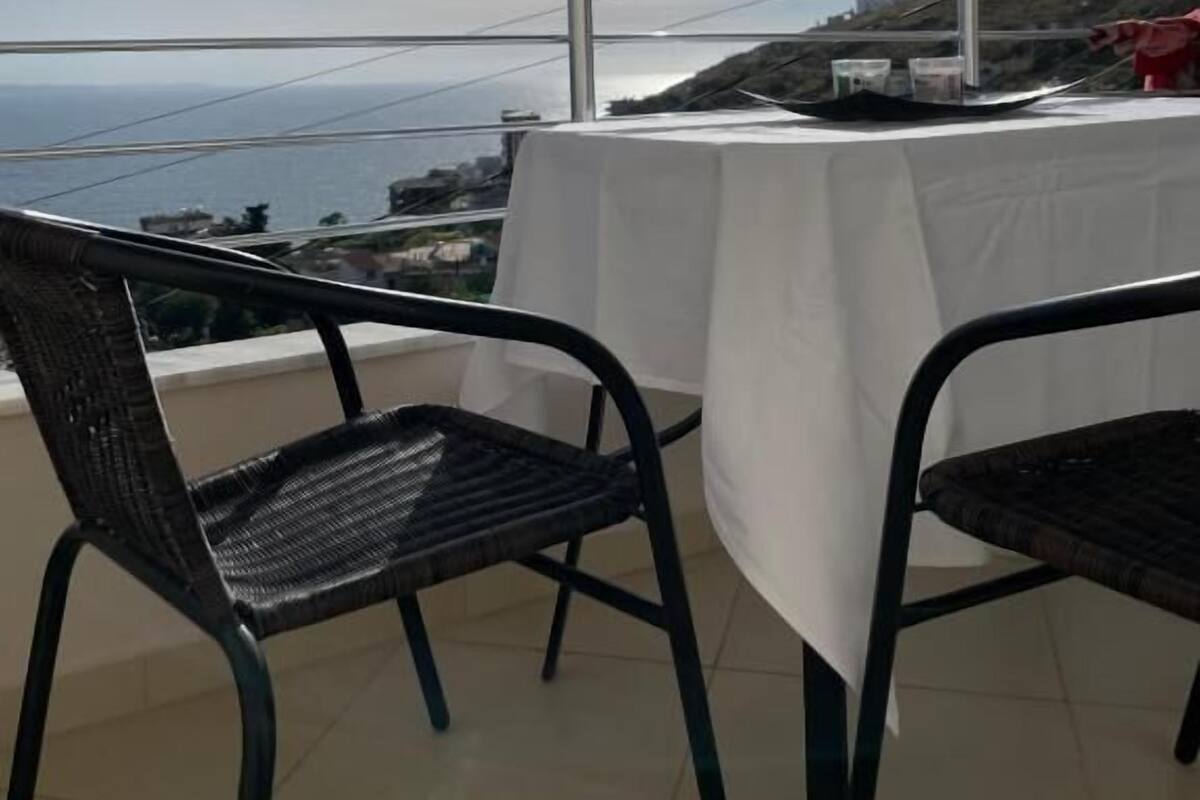 A balcony with a table and chairs, overlooking a coastal landscape.