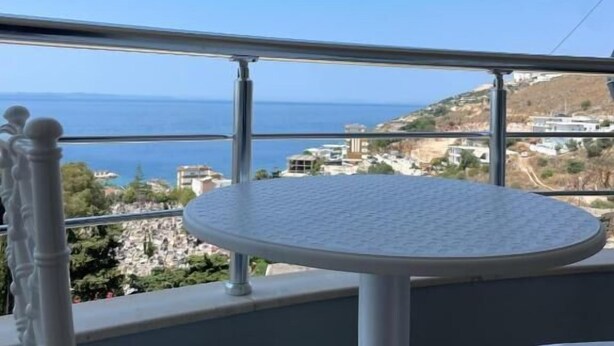 A balcony with a round table and chairs, overlooking a coastal view. - SeaSide Apartments (Sarande)