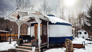 A stationary houseboat with a covered porch, a piano, and a wooden deck.