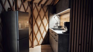 A compact kitchen with a modern refrigerator, wooden beams, a wooden floor, and a countertop with a coffee machine.