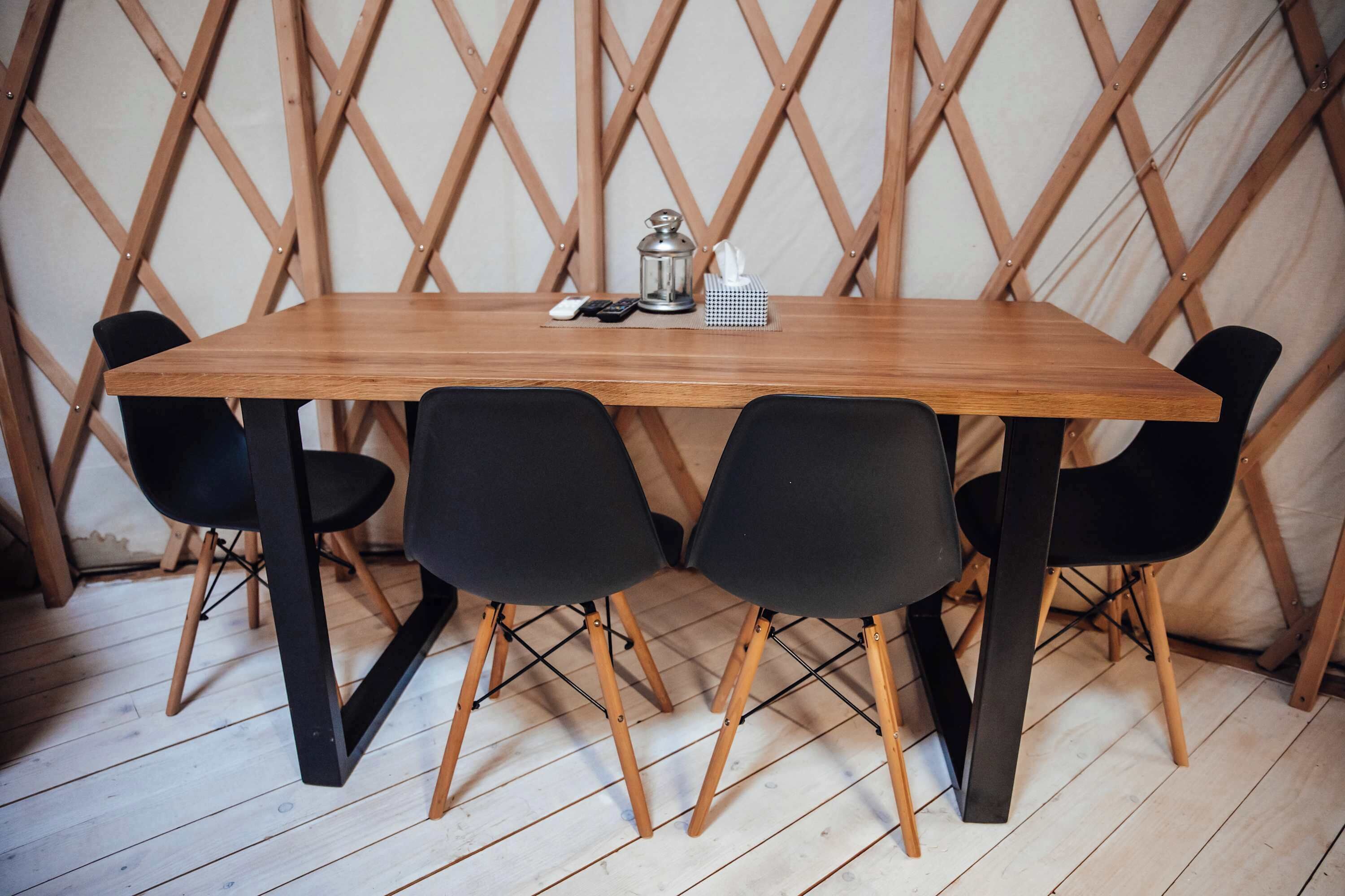 Una mesa de madera con cuatro sillas negras, un pequeño farol de metal y una caja de pañuelos sobre la mesa.