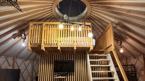 A cozy interior with a wooden slatted ceiling, a balcony with lights, a TV, and a staircase.