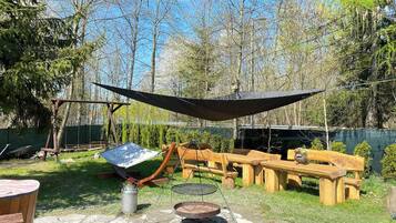 Eine Holzterrasse mit Grilltisch, einer Hängematte und einem Picknicktisch.