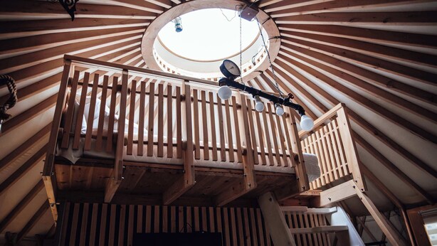 A circular wooden ceiling with a skylight, wooden railings, and a hanging light fixture.