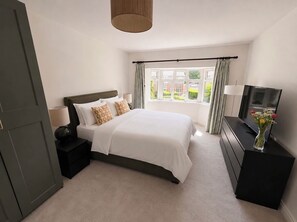 A bedroom with a bed, bedside tables, a dresser, a television, and a window with curtains. - Elegant tranquil family home in Dublin – ideal base for exploring Ireland! (Dublin)