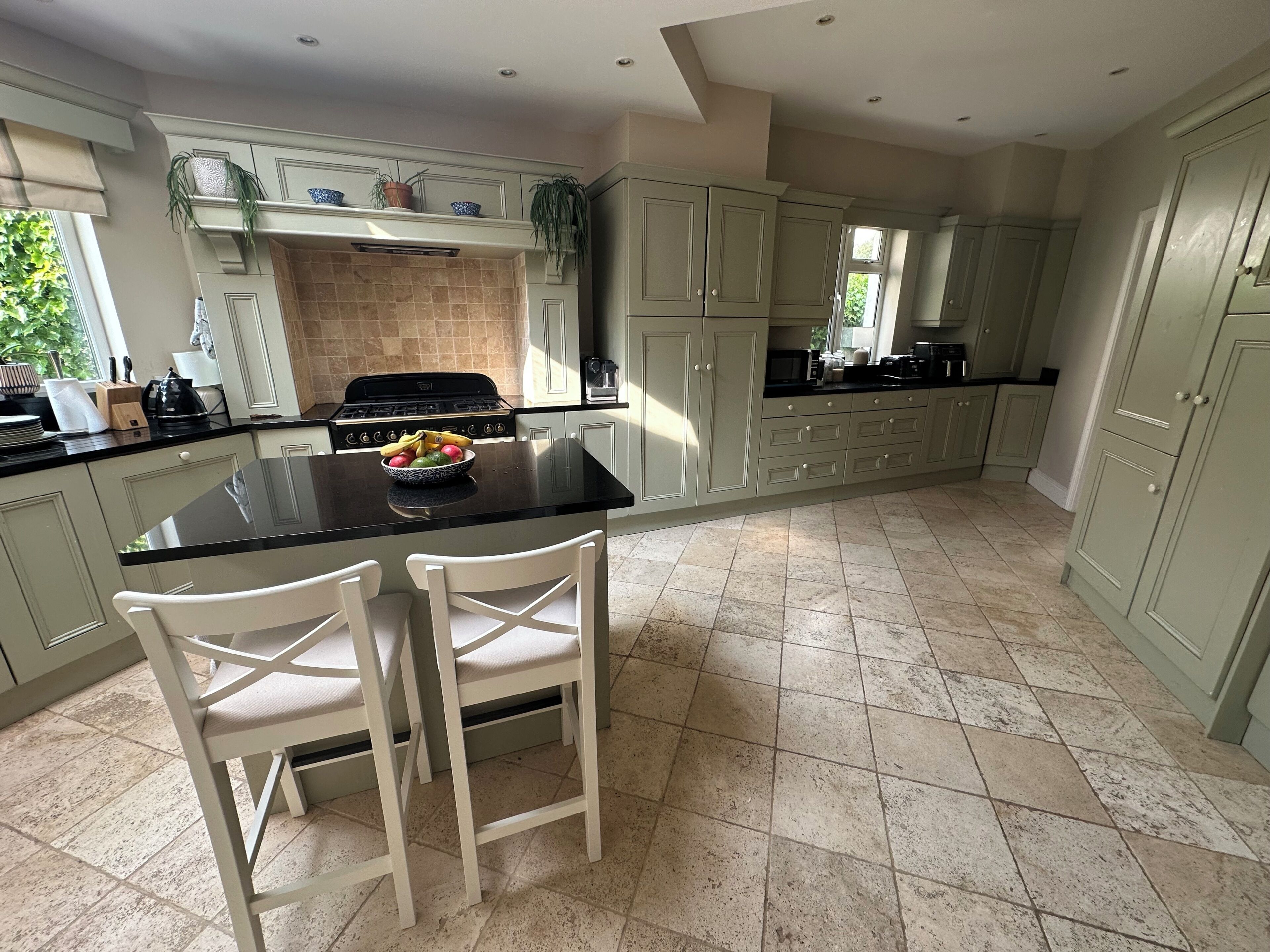 A kitchen with a central island, white chairs, a stove, and cabinets.