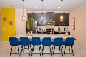 A modern kitchen with a central island, bar stools, and a Mickey Mouse decoration. - Go!#28 Champions Gate (Kissimmee)
