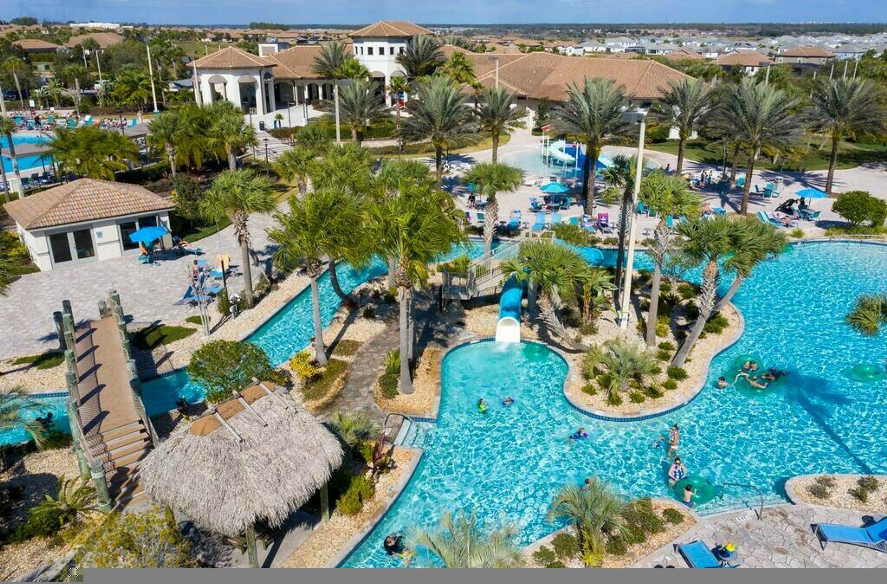 A resort with a large central pool, palm trees, and a thatched-roof building.