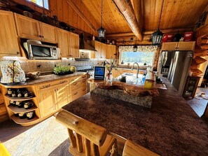 Una cocina rústica con armarios de madera, encimera de granito, microondas, estufa y refrigerador.