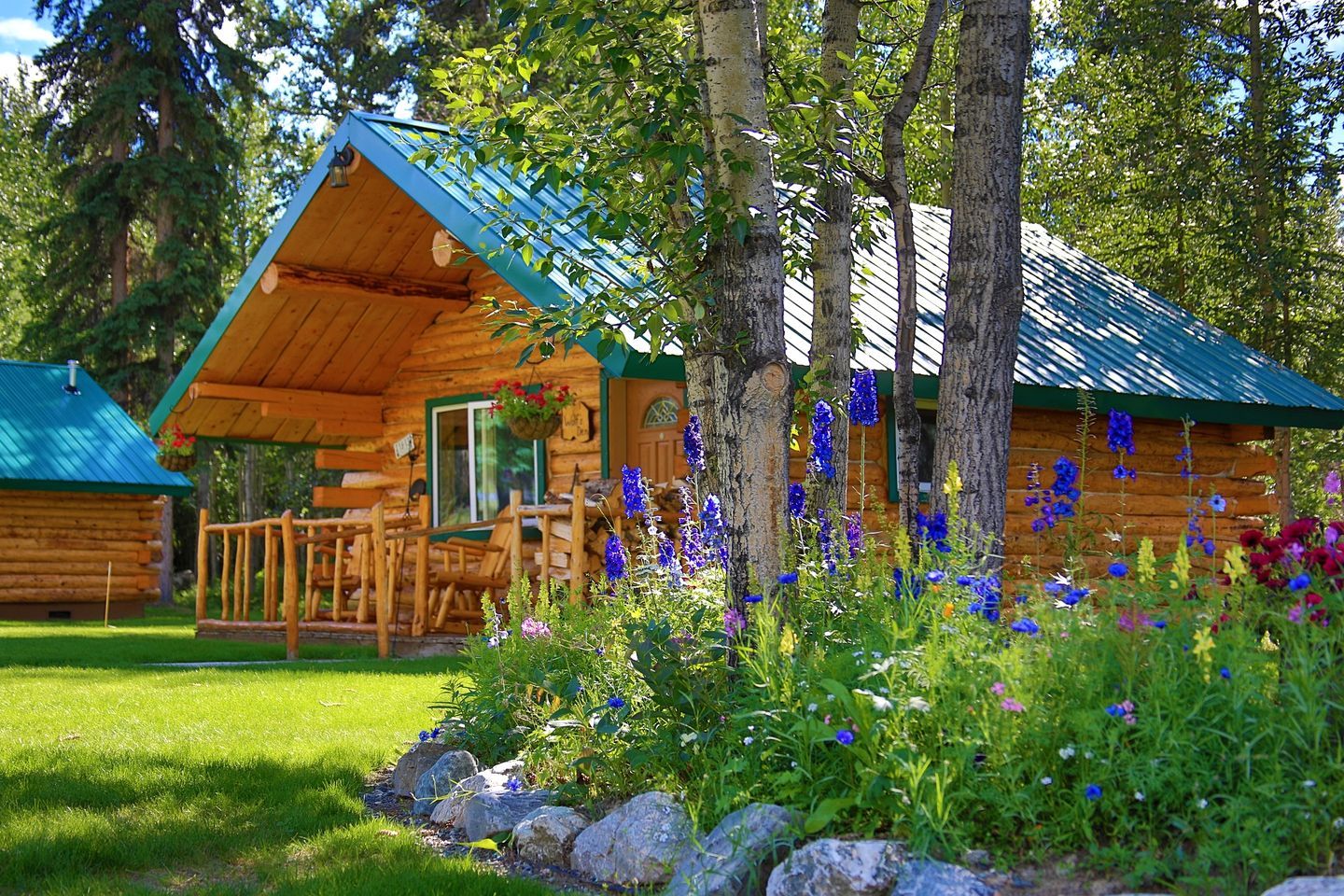 A log cabin with a porch, surrounded by a garden with various flowers and trees.