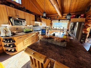 Une cuisine rustique avec des meubles en bois, un plan de travail en granit, un four à micro-ondes, une cuisinière et un réfrigérateur.