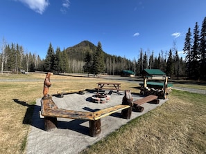 A rustic outdoor seating area with a fire pit, benches, and a wooden sculpture.