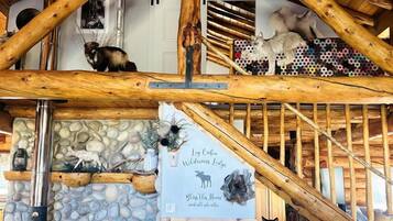 A rustic cabin interior with wooden beams, a stone wall, a fireplace, and a sign indicating it's a wildlife lodge.