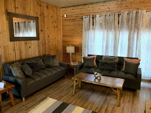 Ein Zimmer mit Holzvertäfelung, zwei Sofas, einem Holztisch und einem gemusterten Vorhang.