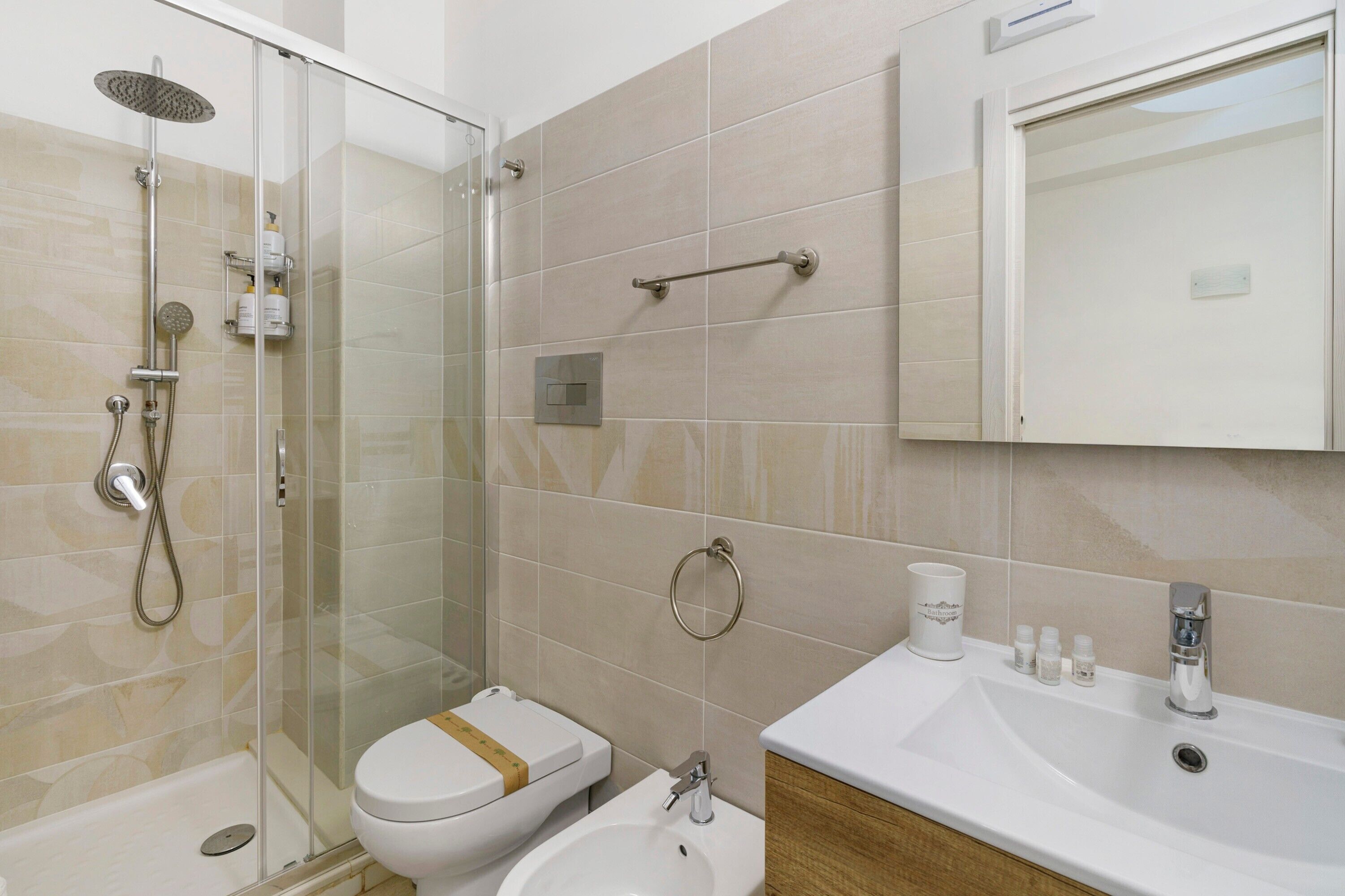 Un baño moderno con ducha de vidrio, inodoro, bidé y lavamanos con artículos de aseo.