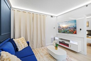Ein modernes Wohnzimmer mit einem blauen Sofa, einem Flachbildfernseher und einem Stadtbildgemälde.