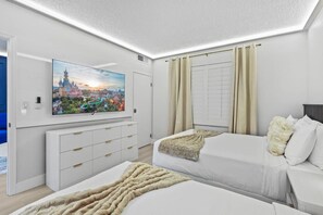 Ein Hotelzimmer mit einem großen Flachbildfernseher, zwei Betten, einer weißen Kommode und einem Fenster mit Vorhängen.
