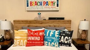 Ein Bett mit Kissen mit Strandmotiven, ein Poster an der Wand und eine aufwendige Handtuchgestaltung auf dem Bett.