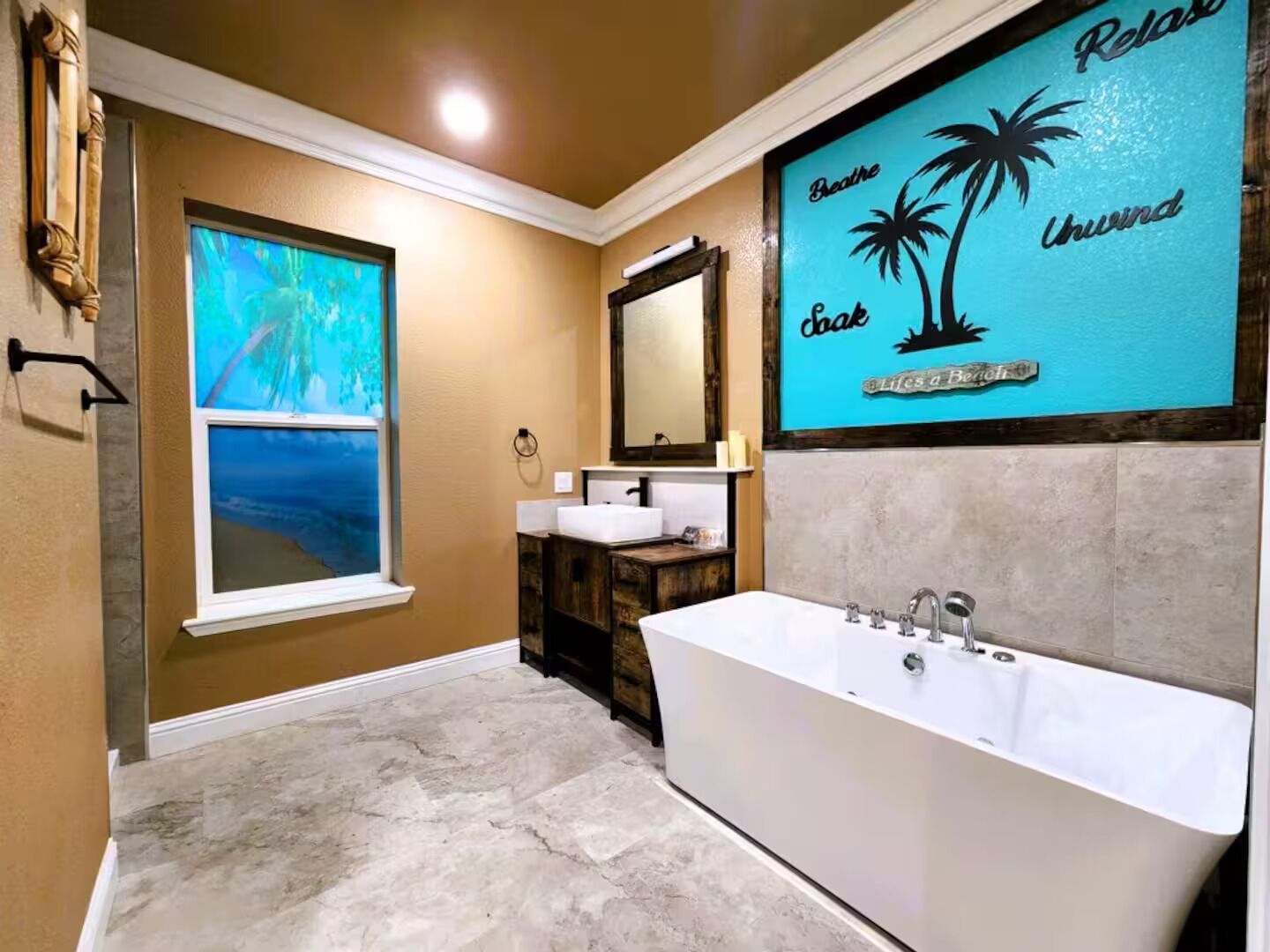 Ein Badezimmer mit einer Badewanne, einem Fenster mit Ausblick, einem Waschtisch mit Spiegel und einer Wand mit tropischem Kunstwerk.
