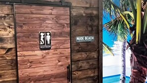 Eine Holzwand mit einem Schild für die Toilette und einem Schild mit der Aufschrift 'NUDE BEACH'.