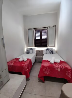 Una habitación de hotel pequeña y moderna con dos camas, una mesita de noche, un espejo y una ventana con persianas.