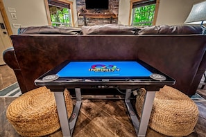 Ein Gaming-Tisch mit Infinity-Logo, ein Steinkamin, eine Ledersofa und gewebte Poufs.