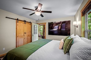 Une chambre à coucher avec un lit, un ventilateur de plafond, une porte en bois, une fenêtre et un tableau accroché au mur.