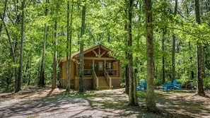 Eine Holzblockhütte, umgeben von einem Wald, mit einer Veranda und Sitzgelegenheiten im Freien.