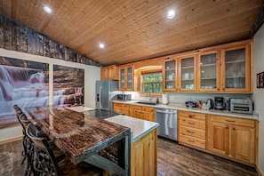 Eine Küche mit Holzausstattung, einem Edelstahl-Kühlschrank, einem Geschirrspüler und einer Arbeitsplatte aus Granit.