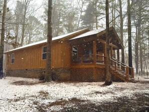 Eine Holzhütte mit Veranda und Treppe, umgeben von Bäumen.