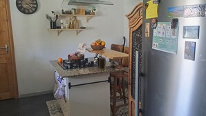 A compact kitchen with a built-in gas stove, wooden shelves, a bowl of fruit, and a refrigerator with magnets and notes. - Cozy house with a garden and pool in Carpentras (Carpentras)